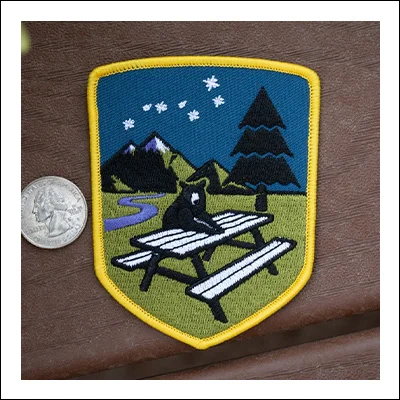 Embroidered patch featuring a bear at a picnic table